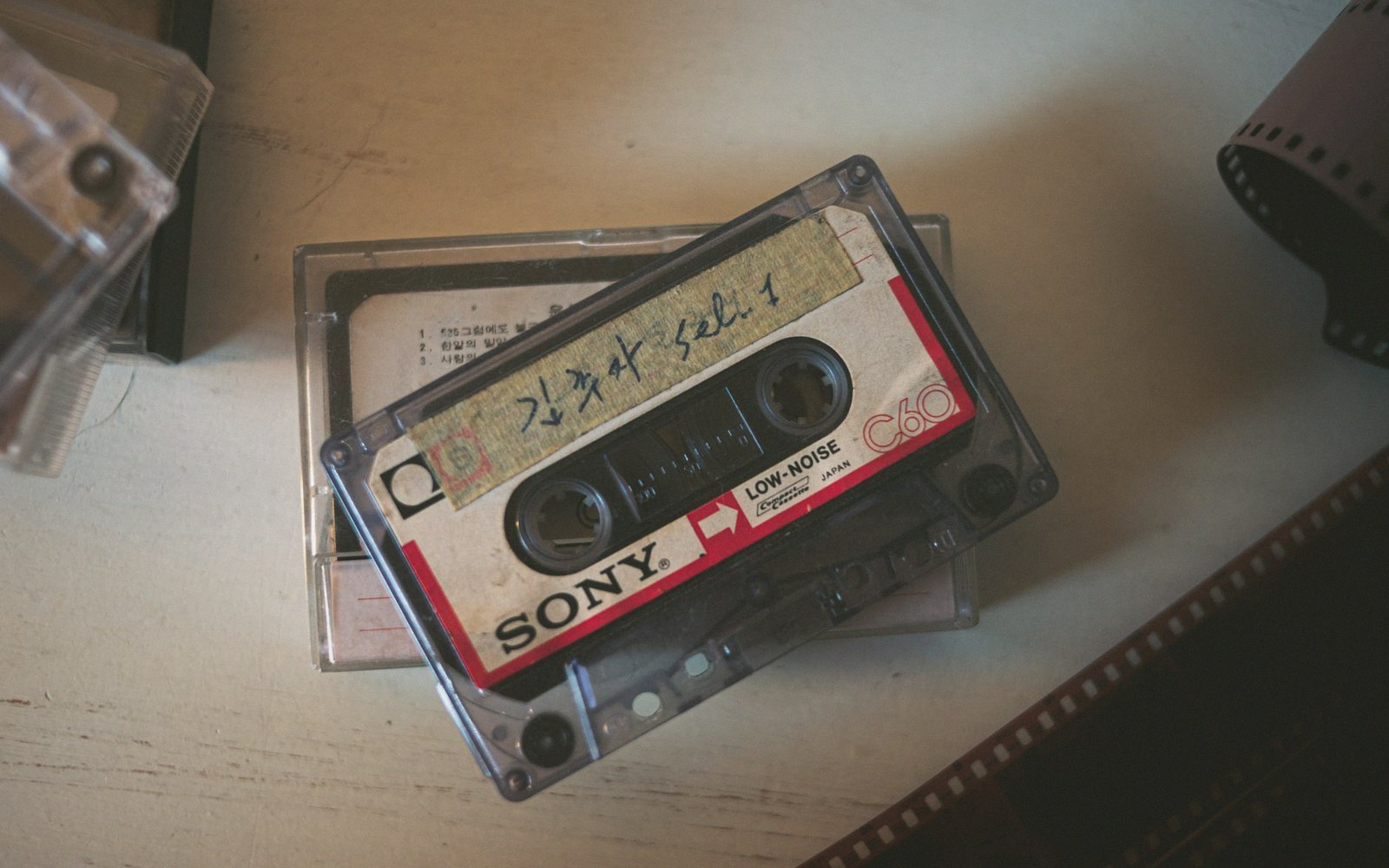 A C-60 cassette tape with a hand-typed paper label, lying on a wooden surface next to a folded photocopied insert