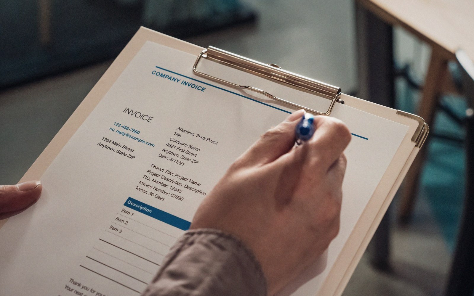 A hand holding a pen fills out a company invoice on a clipboard