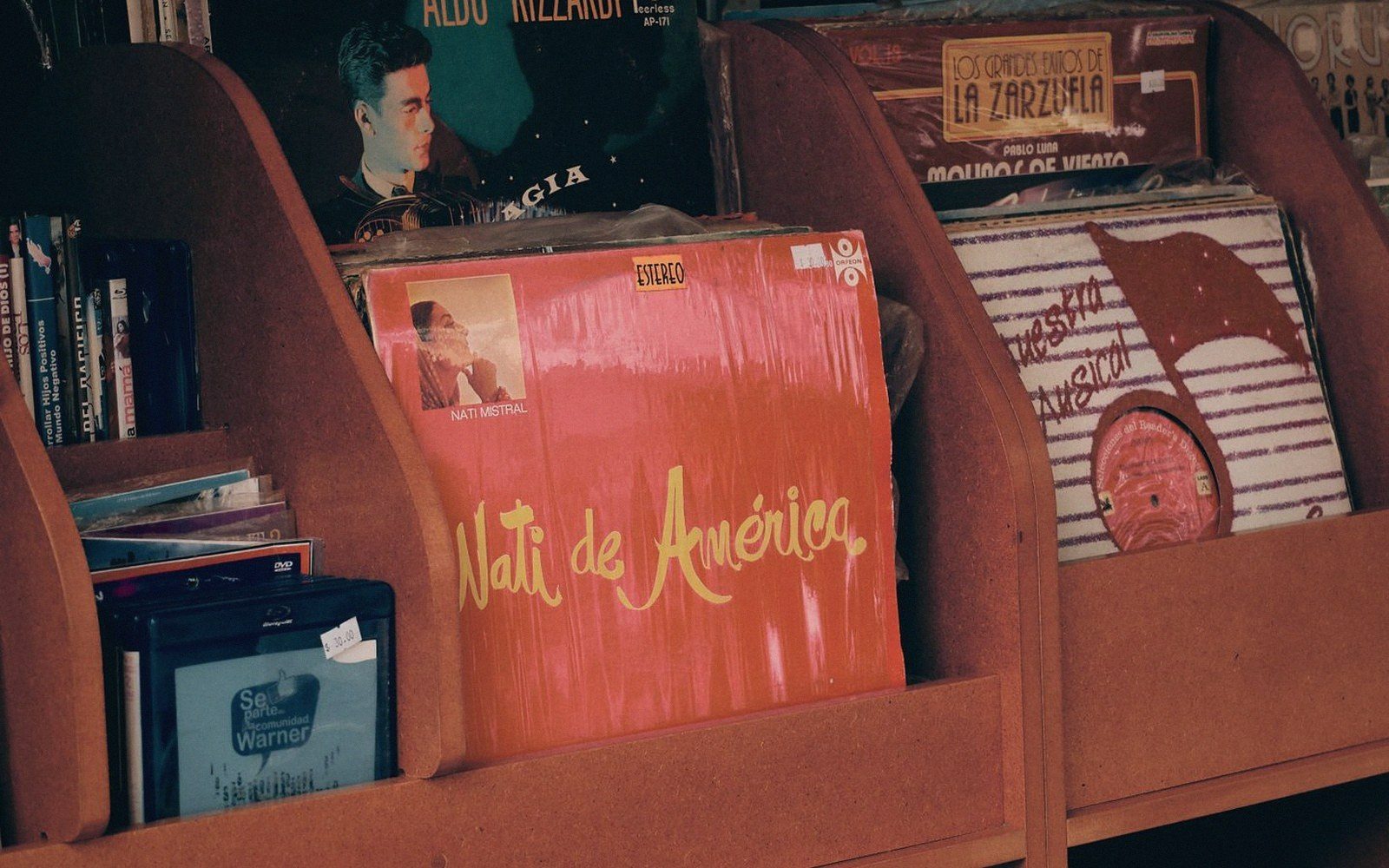 Vinyl records including "Nati de América" displayed upright in wooden shop bins