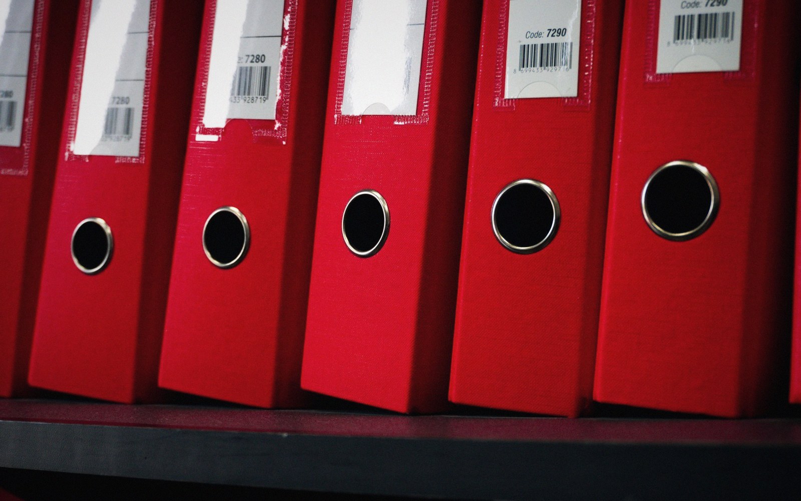 Red ring binders with barcode labels lined up on a shelf