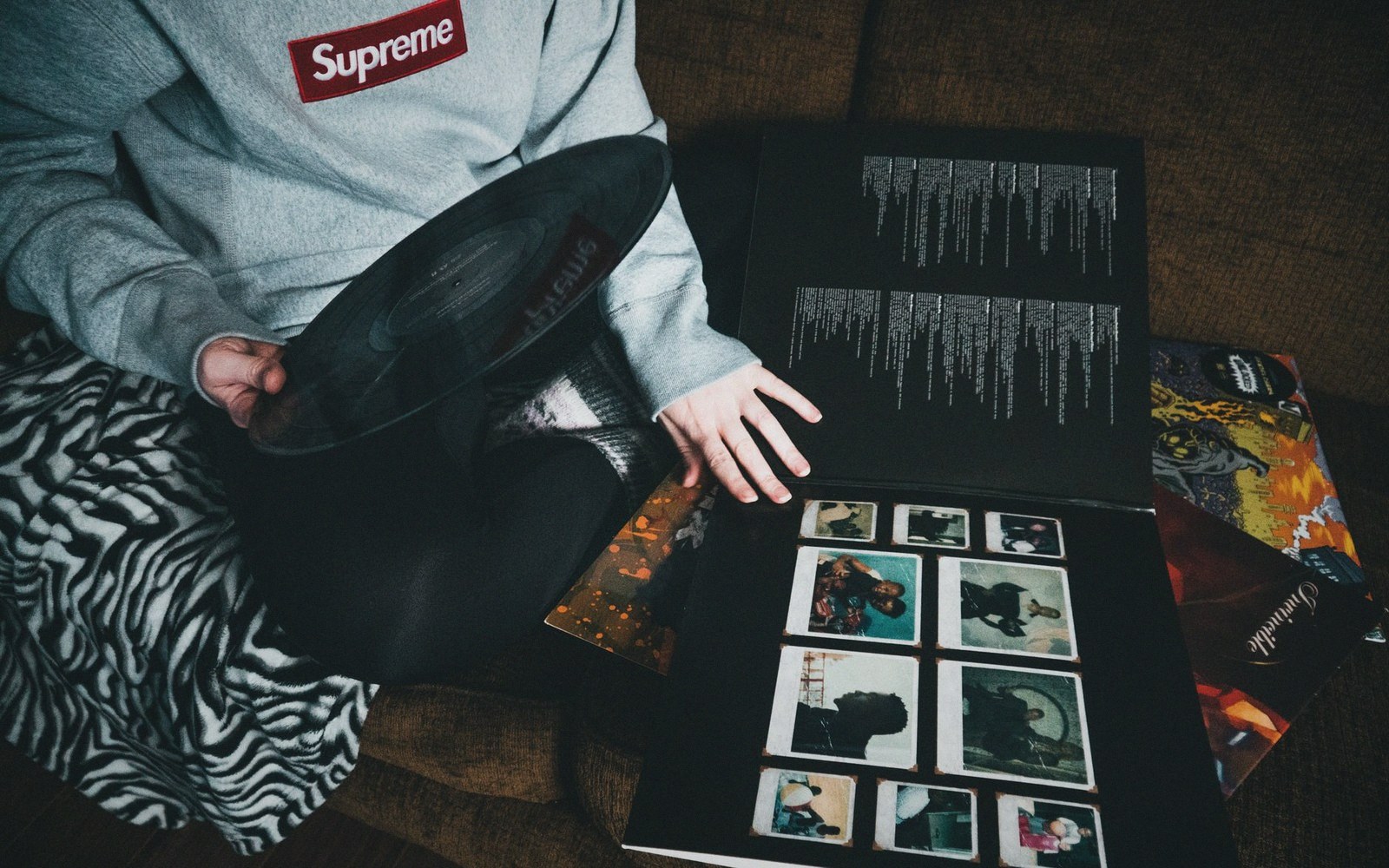 Person holding a vinyl record beside an open album sleeve with photo prints