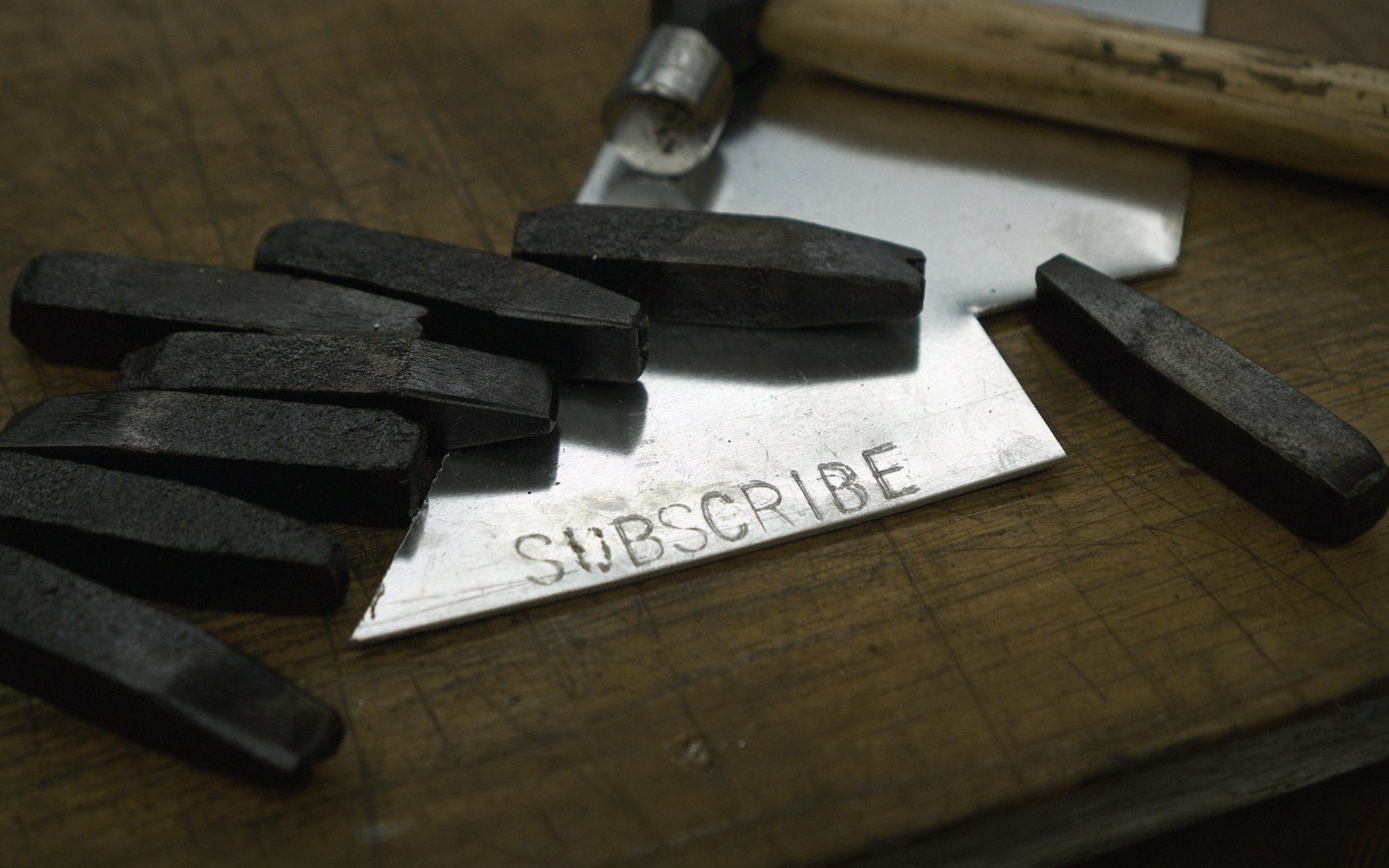 Metal letter stamps and a hammer beside a stamped strip reading "subscribe"