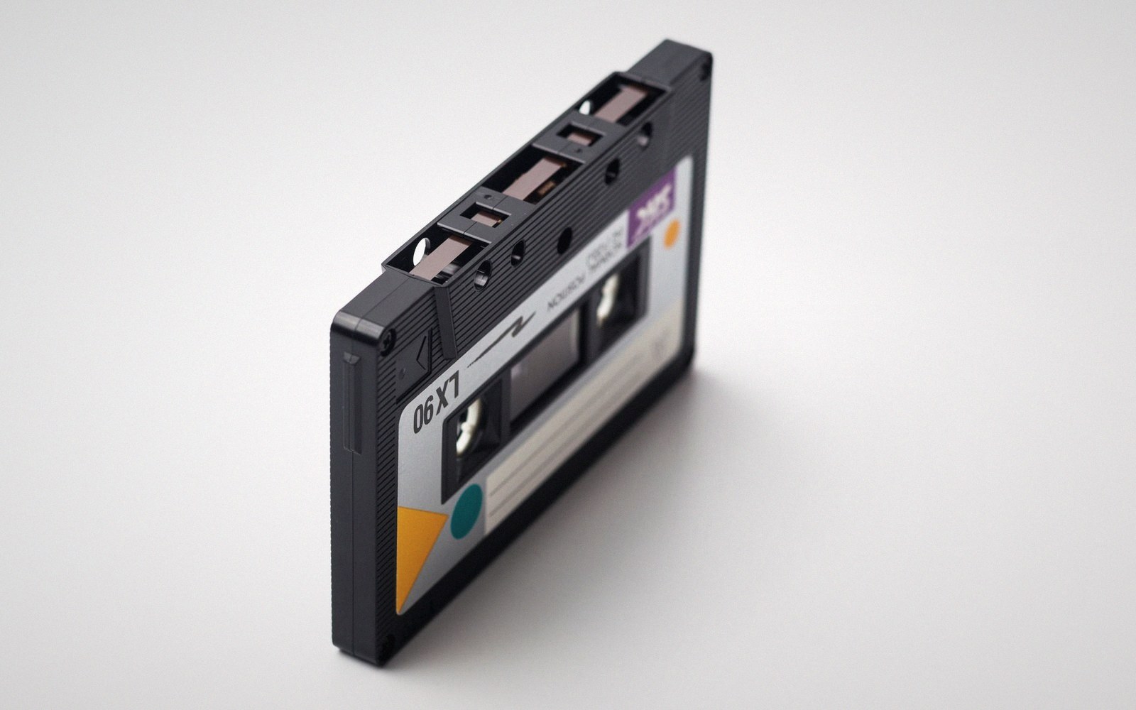 A black cassette tape standing upright on a plain light gray surface