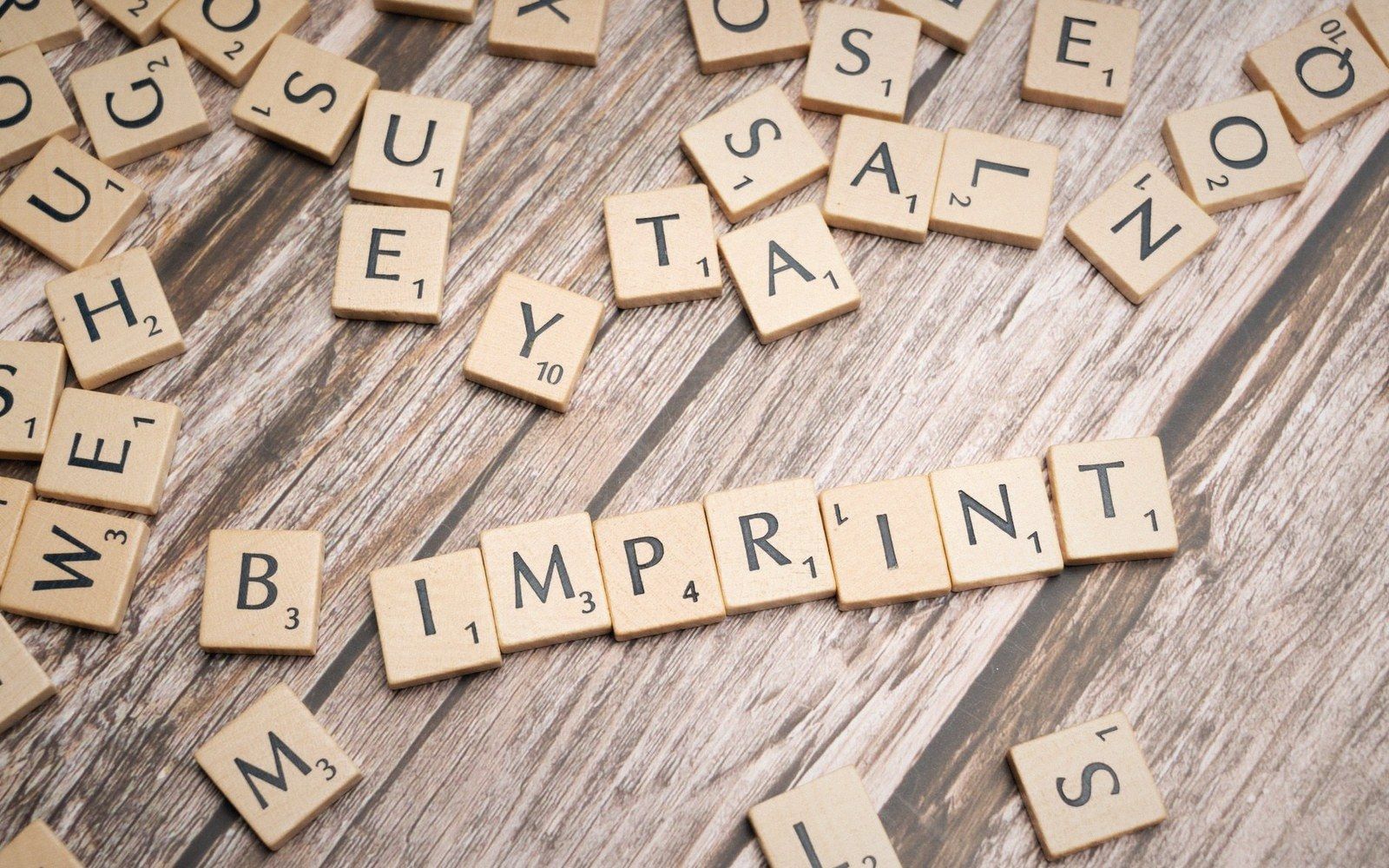 Scrabble tiles spelling "imprint" arranged on a weathered wooden surface