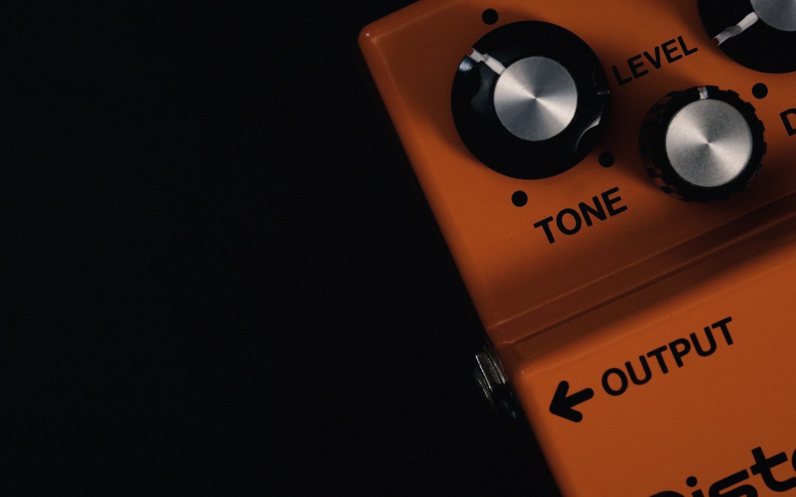 Close-up of an orange guitar distortion pedal with tone and level knobs
