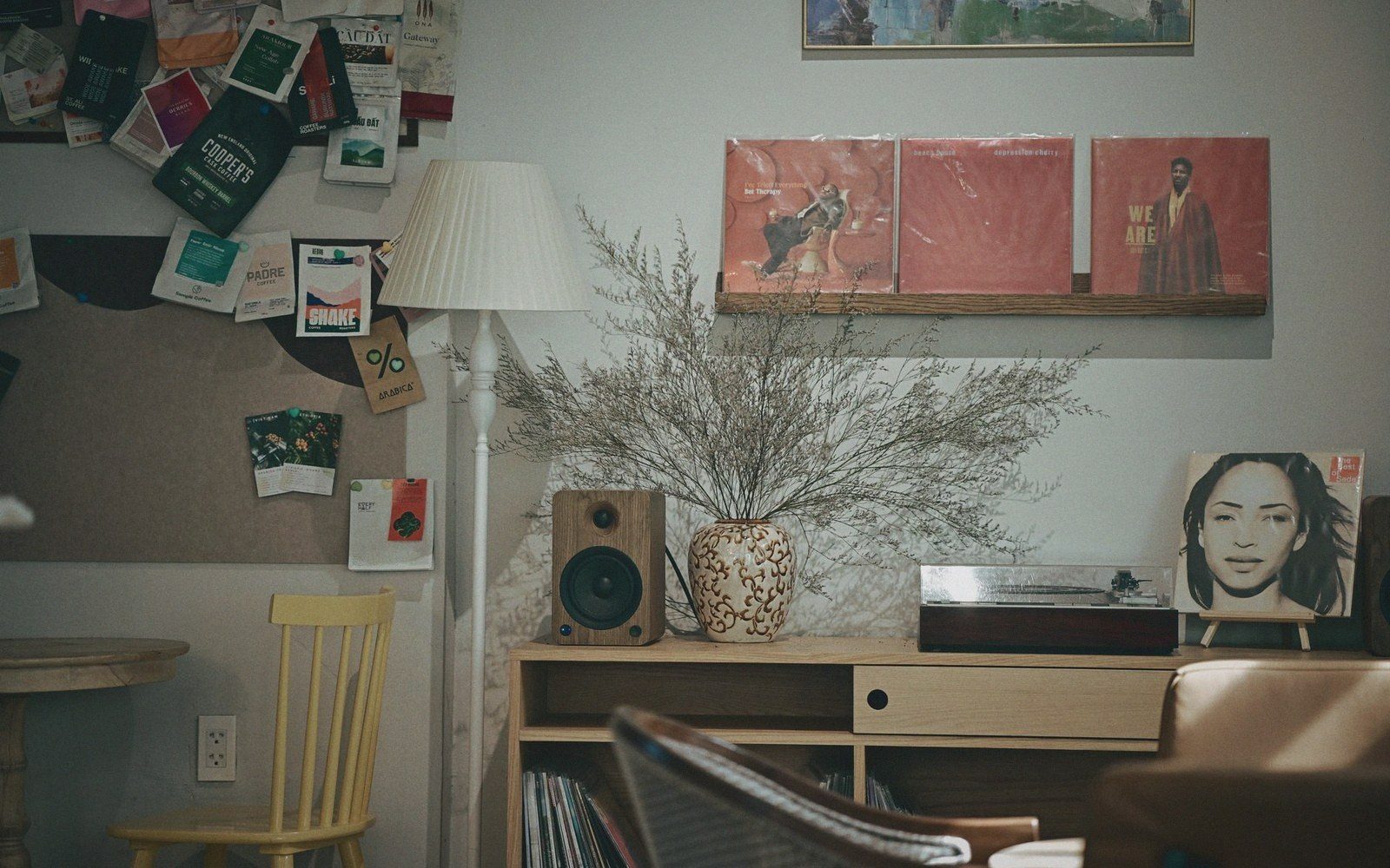 Vinyl records displayed on a wall shelf above a wooden cabinet with speaker and vase