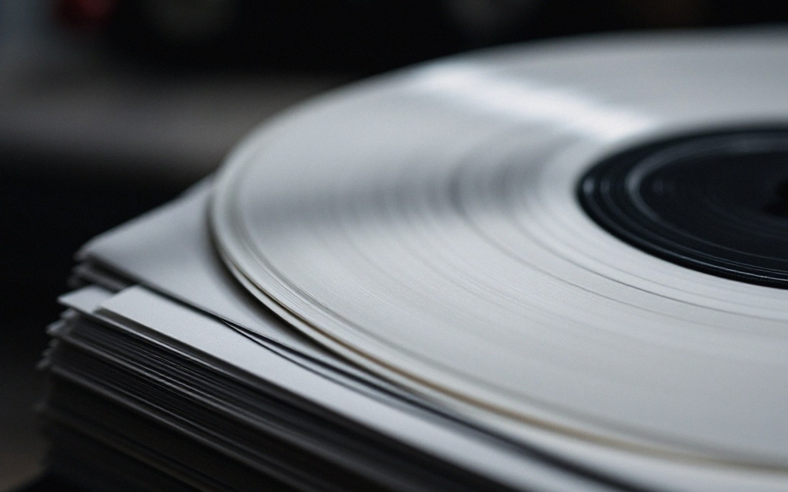 A stack of twelve-inch records in white paper inner sleeves, edges facing camera, spines of the outer jackets visible at the back